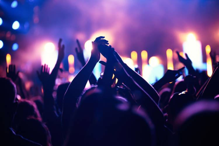 Festival-goers jam out to live music festival-goers facing concert stage with hands in the air