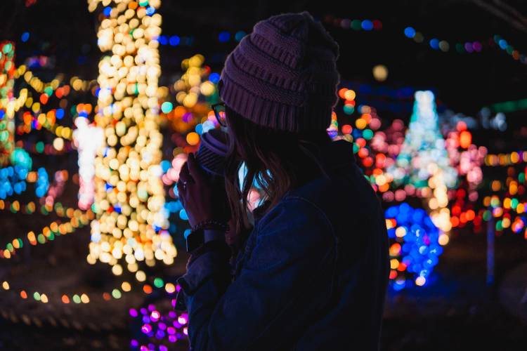 woman with hot chocolate looking at outdoor holiday lights