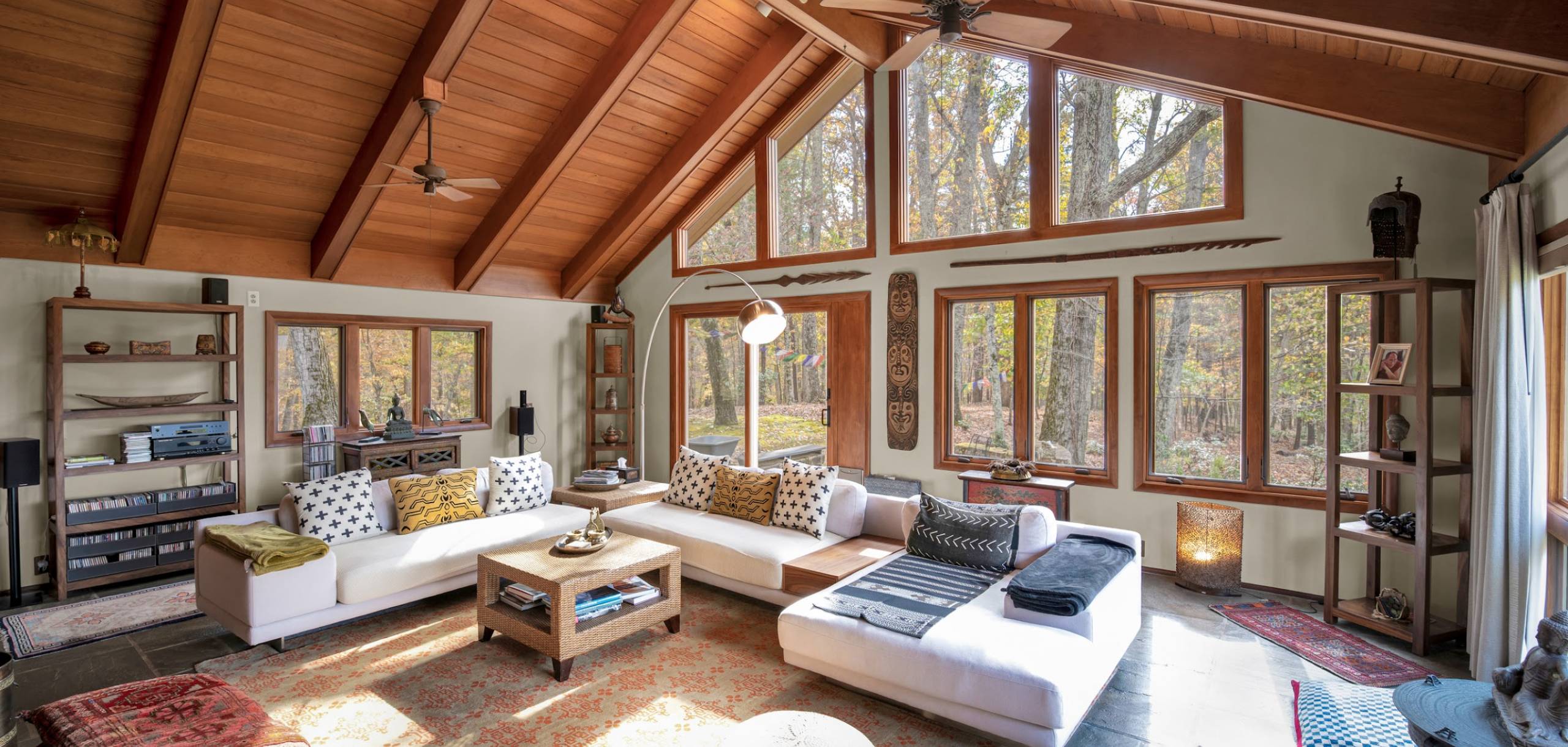 Vaulted ceilings with exposed wood beams over a large living space with many windows and large white sectional sofa