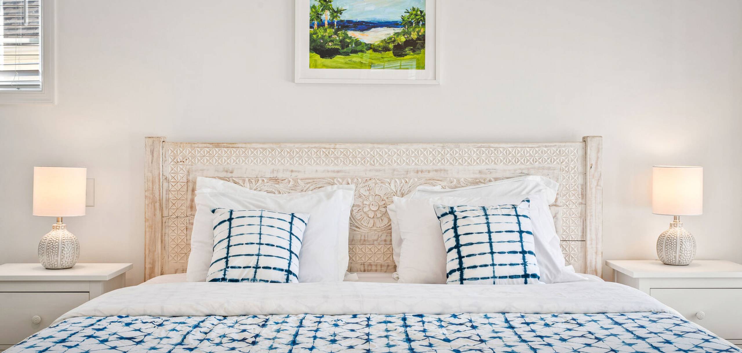 King bed with blue bedding and small green and blue artwork above it